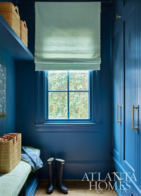 Blue mudroom with a window, bench, baskets, and tall cabinets with brass hardware.