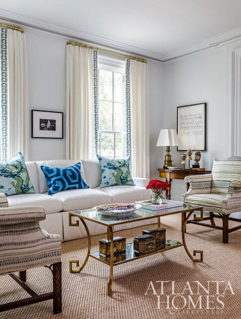 White sofa with patterned pillows, glass coffee table, and striped armchair.