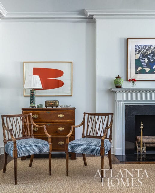 Two armchairs with blue patterned seats in front of a wooden chest and fireplace.