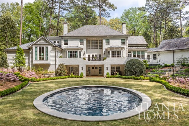 White brick house with gray roof, circular pool, and manicured lawn.