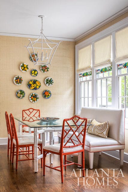 Dining room with orange bamboo chairs, glass table, and fruit-themed wall plates.