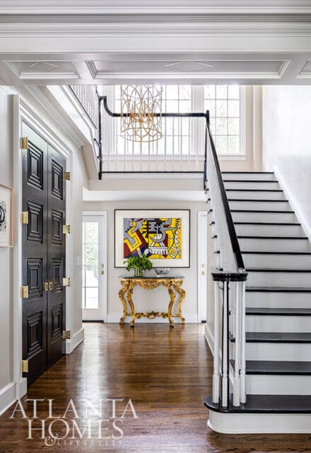 Foyer with black paneled doors, gold console table, pop art, and black and white staircase