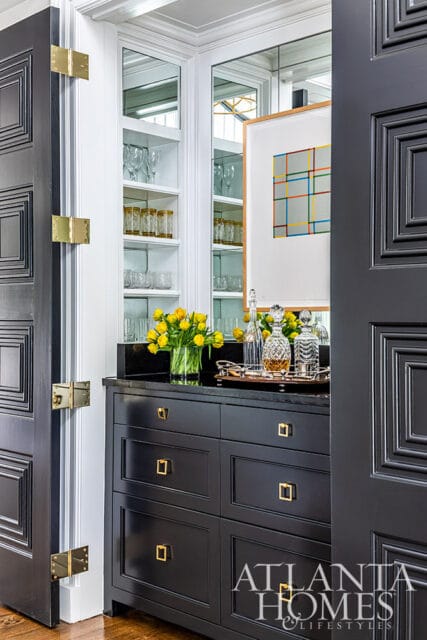 Black built-in bar with glass shelves, decanters, and yellow tulips.
