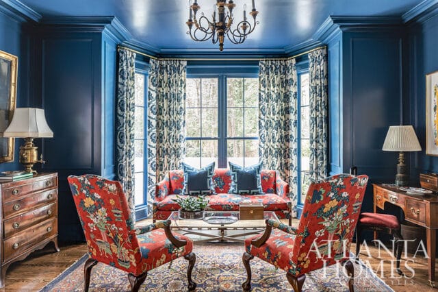 Blue room with floral chairs and sofa, paneled walls, and patterned curtains.