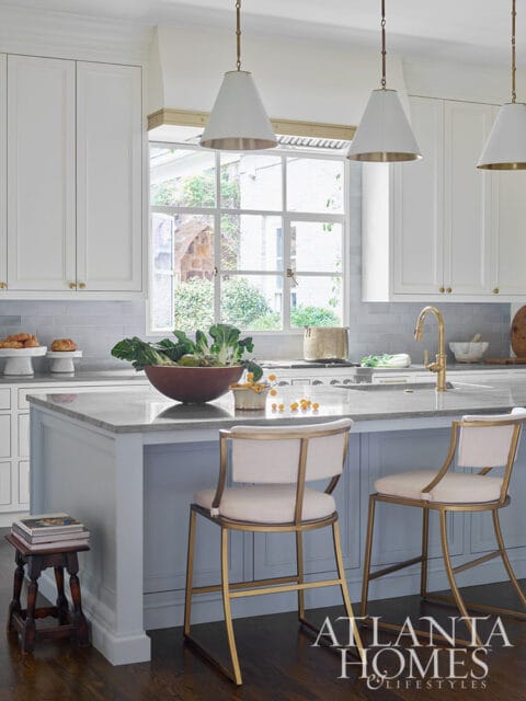 White kitchen with gray tile backsplash, marble island, and brass accents.
