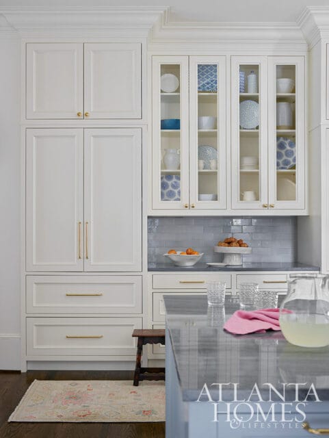 White kitchen cabinets with glass doors displaying blue and white patterned dishes, gray subway