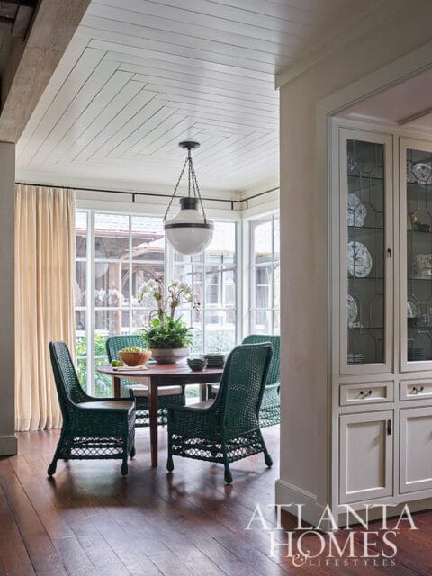Dining room with dark wood floors, green wicker chairs, and a round table.