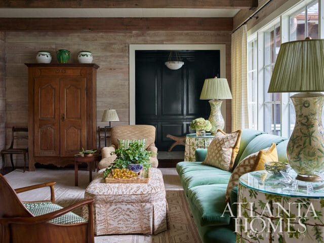 Living room with teal sofa, patterned ottoman, wooden armoire, and Atlanta Homes & Lifestyles logo.