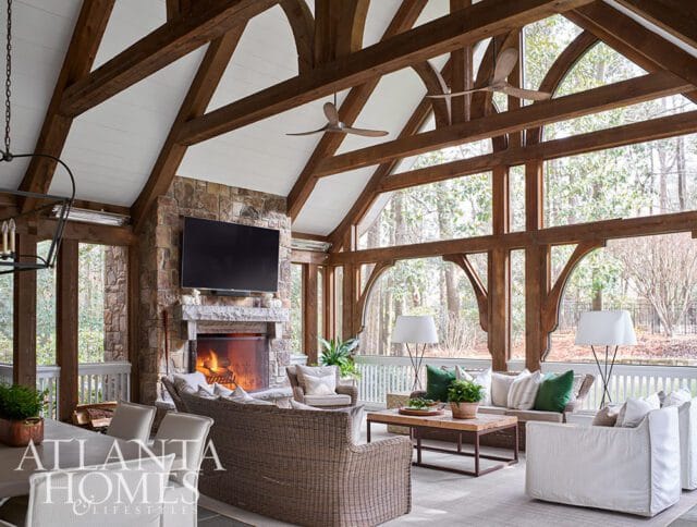 Screened porch with stone fireplace, wicker furniture, and wood beams