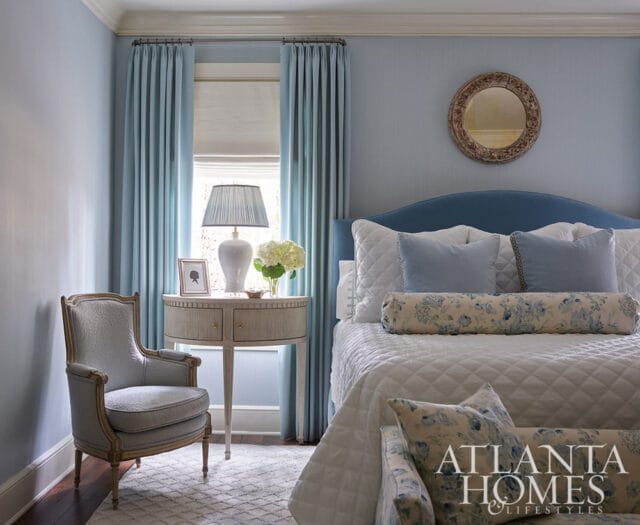 Blue bedroom with upholstered headboard, white quilted bedding, and floral pillows.