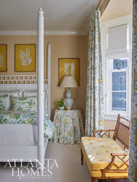 Bedroom with white four-poster bed, yellow botanical print curtains, and yellow bench.