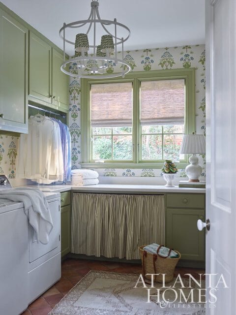 Green laundry room with white washer, patterned wallpaper, and striped curtain.