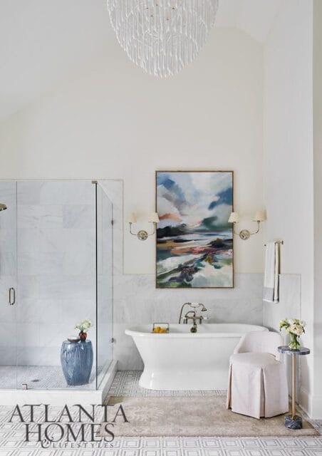 White bathroom with marble shower, freestanding tub, abstract art, and chandelier.
