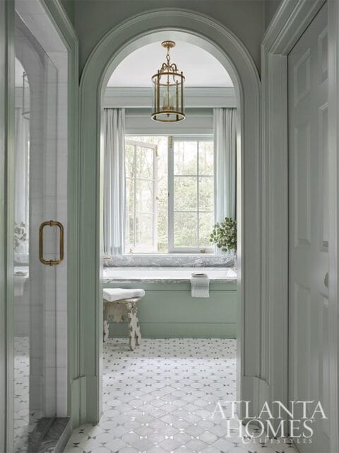 Pale green bathroom with marble bathtub, brass lantern, and patterned tile floor.