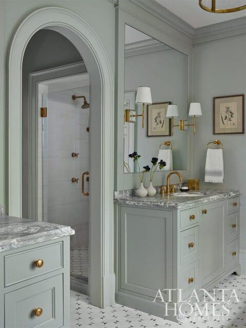 Gray bathroom vanity with marble countertop and brass hardware, arched doorway to shower.