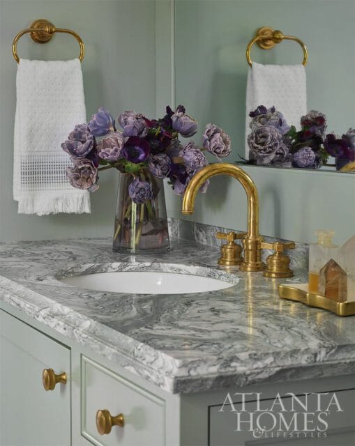 Powder room with marble vanity, gold faucet, and purple floral arrangement.