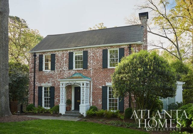 Red brick house with dark shutters and white trim porch. Atlanta Homes & Lifestyles logo in lower