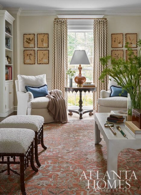 Living room with white armchairs, patterned curtains, and a floral rug.