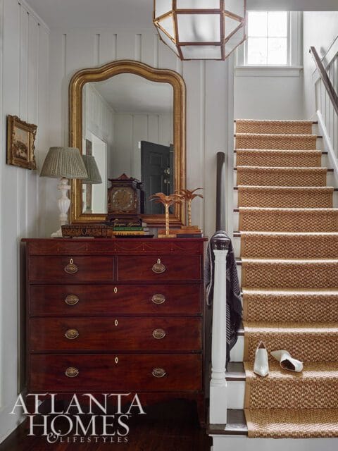 Mahogany dresser with brass hardware, gold mirror, and sisal runner on stairs.