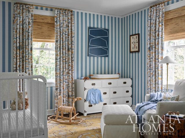 Nursery with blue striped walls, patterned curtains, white crib, changing table, and armchair.