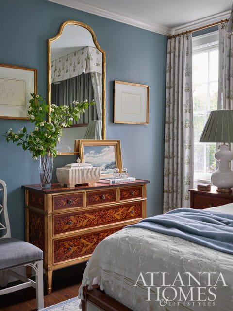 Blue bedroom with ornate dresser, gold mirror, floral curtains, and Atlanta Homes & Lifestyles logo.