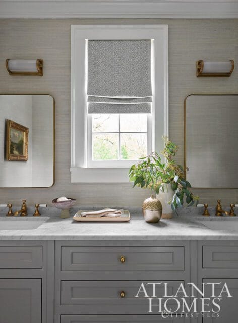 Gray bathroom vanity with marble countertop, brass fixtures, and textured wallpaper.
