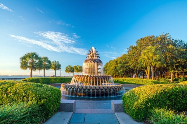 Pineapple fountain with water cascading down, surrounded by manicured hedges and palm trees.