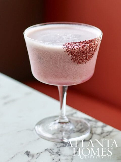 Pink cocktail with a rim of red sugar garnish in a coupe glass.