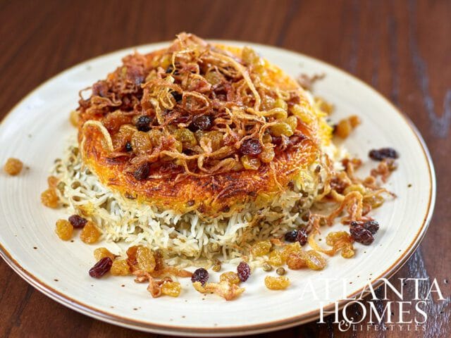 Rice and lentil dish topped with fried onions and raisins on a white plate.