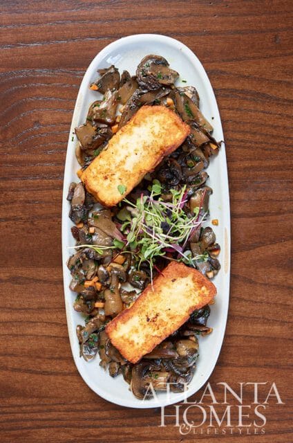Fried halloumi cheese slices on a bed of sautéed mushrooms and microgreens.