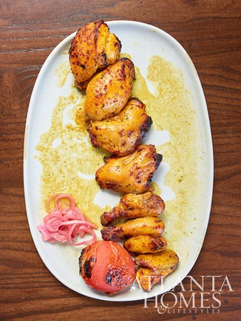 Grilled chicken skewers with pickled onions and a roasted tomato on a white platter.