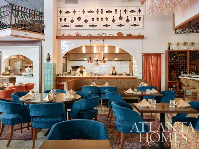 Restaurant dining room with blue velvet chairs, wood tables, and an open kitchen.