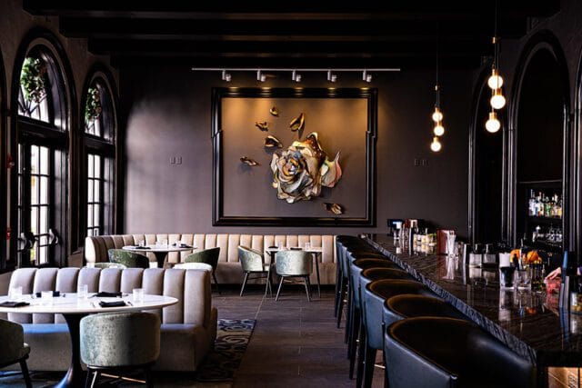 Dark bar with granite counter, black stools, and plush banquette seating.