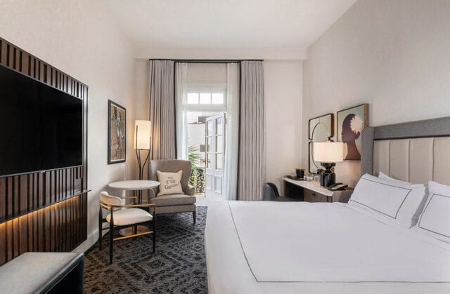 King bed with white linens, gray upholstered headboard, and a desk with a lamp.