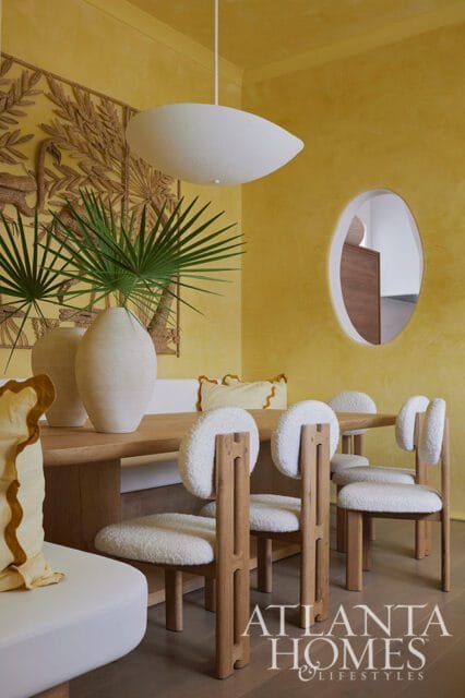 Yellow dining room with wooden table, white textured chairs, and oval mirror