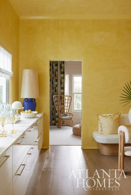 Yellow room with marble countertops, white cabinetry, and a large lamp. A doorway reveals a wicker