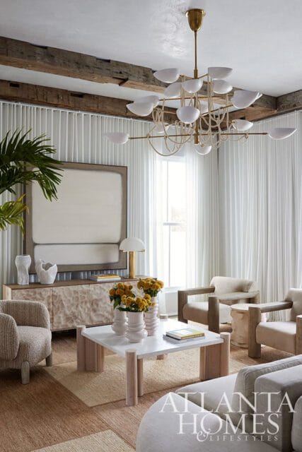 Living room with white curtains, exposed wood beams, abstract art, and modern furniture.