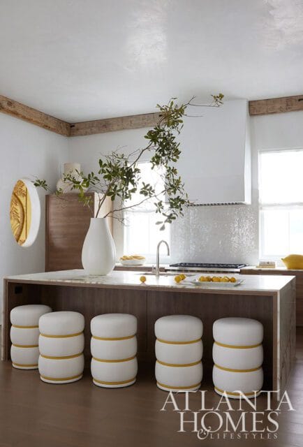 Kitchen island with white stools, marble countertop, and a large vase with branches.