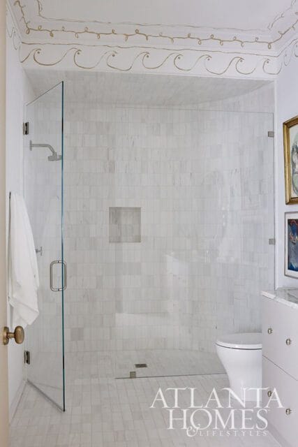 White marble tiled bathroom with glass shower enclosure, toilet, and decorative wave border on