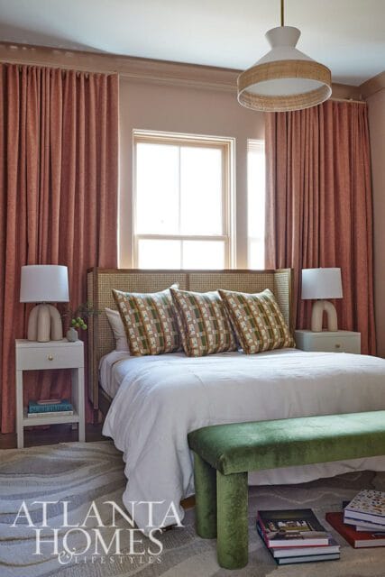 Bedroom with coral curtains, cane headboard, patterned pillows, and white bedding.