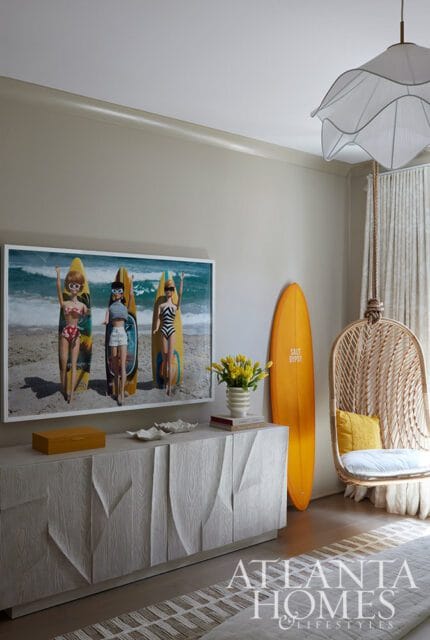 Living room with surfboard art, rattan hanging chair, and textured credenza.