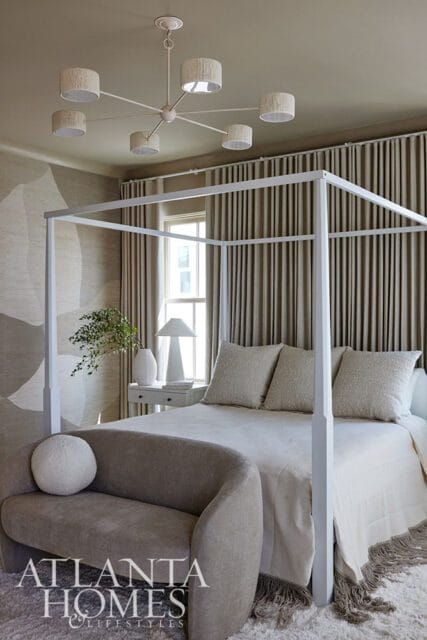 Bedroom with white canopy bed, neutral bedding, textured wallpaper, and gray curved bench.