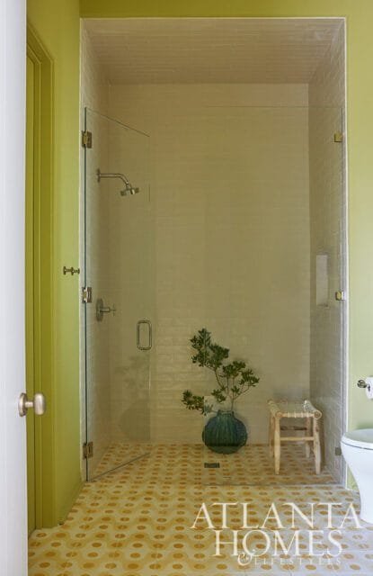 Shower with glass doors, subway tile walls, patterned floor, and a green vase with a plant.