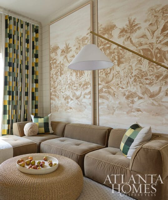 Brown sectional sofa with patterned pillows, large botanical mural, and woven ottoman with fruit