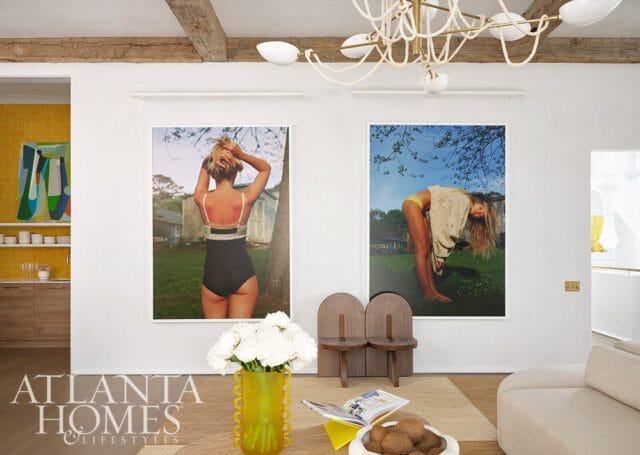 Living room with two framed photos of women, yellow vase with white flowers, and beige sofa.
