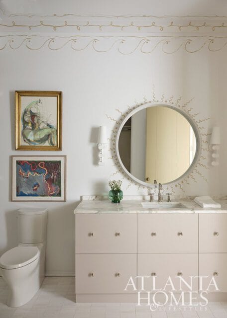 Bathroom with beige vanity, marble countertop, round mirror, and two abstract paintings above