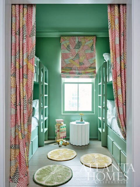Green bunk room with patterned curtains, lime and lemon rugs, and a white side table.