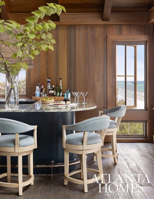 Bar with light blue upholstered stools, granite countertop, and wood paneled walls overlooking the