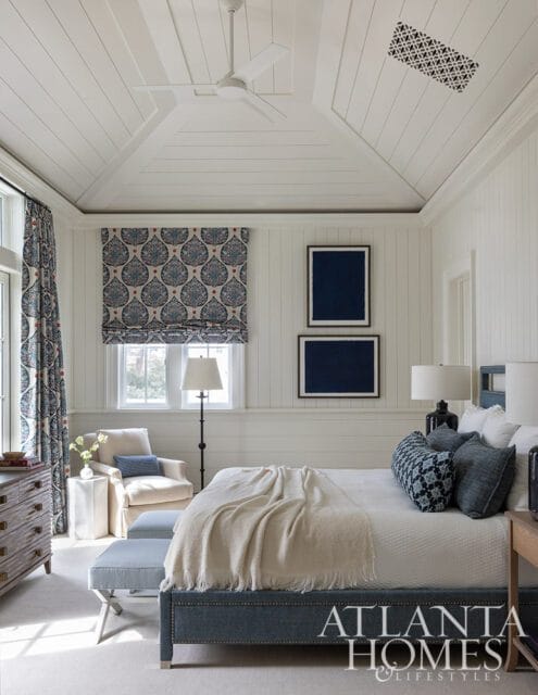 Bedroom with white paneled walls and ceiling, blue patterned curtains and pillows, and a blue
