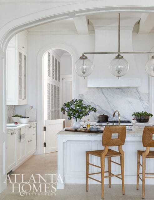 White kitchen with marble backsplash, island, and woven bar stools.